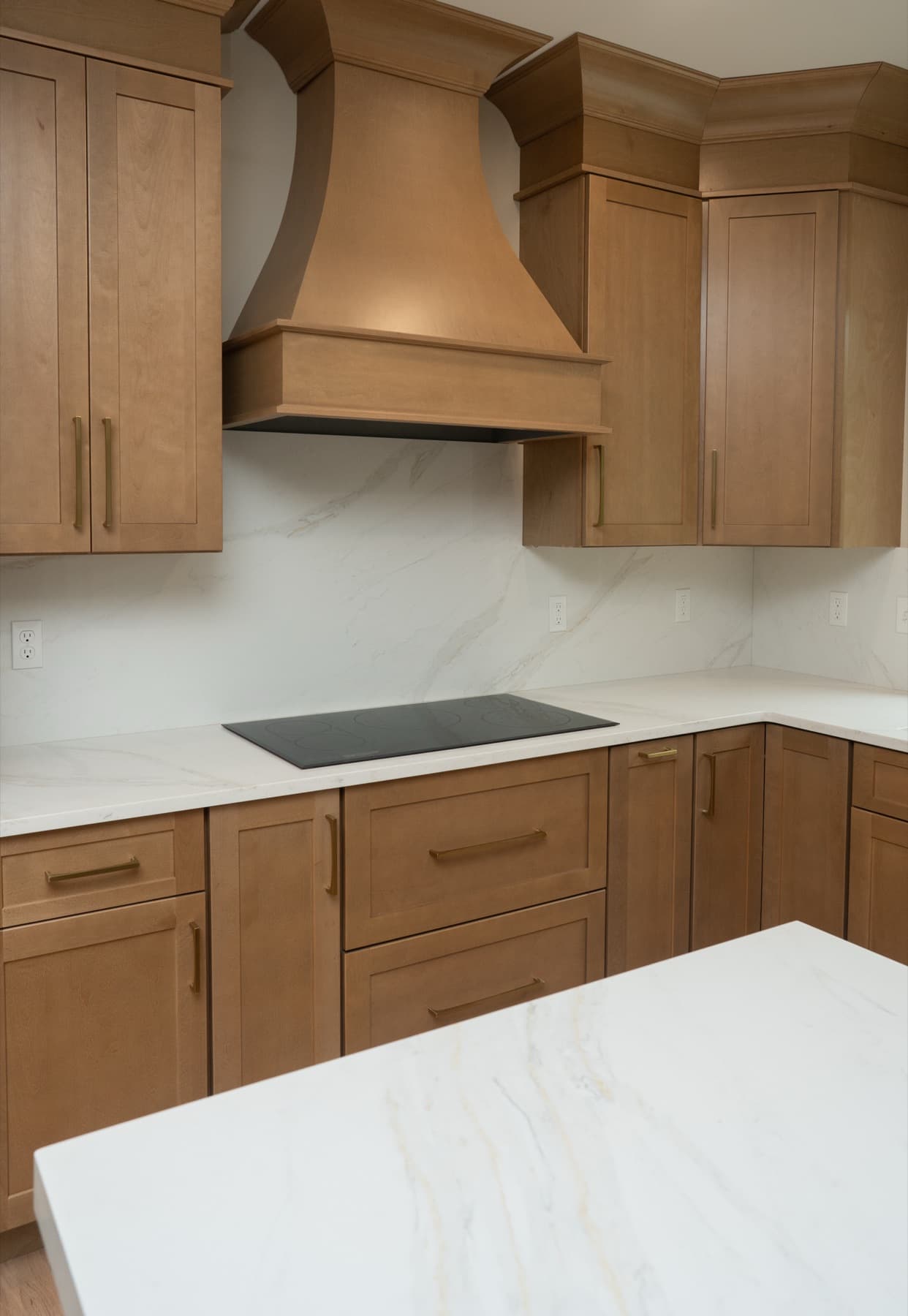Curved wood range hood above a cooktop with Calacatta Silverlight counters and backsplash