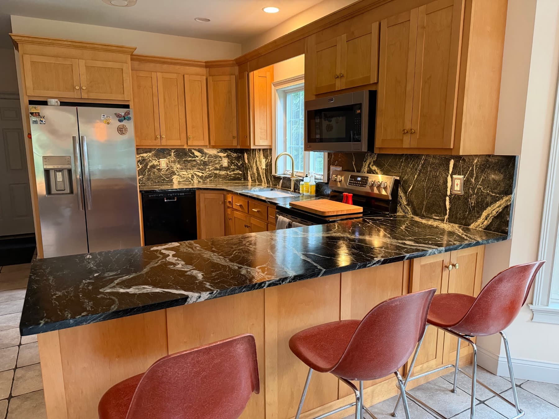 Kitchen peninsula with dark Grey Venato countertops with white veining and maple cabinets