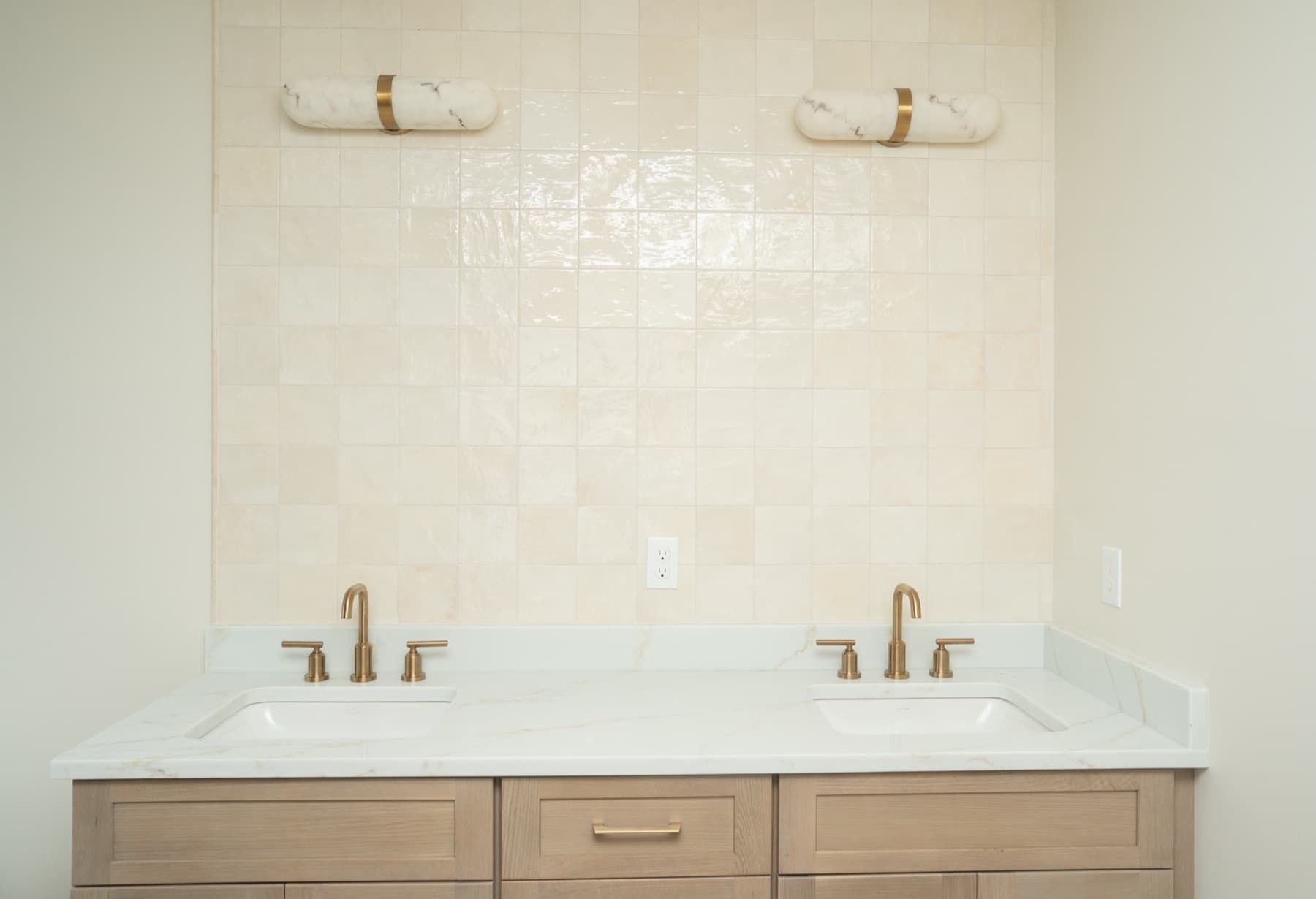 Double vanity with Jasper quartz top against a cream zellige tile wall with brass sconces