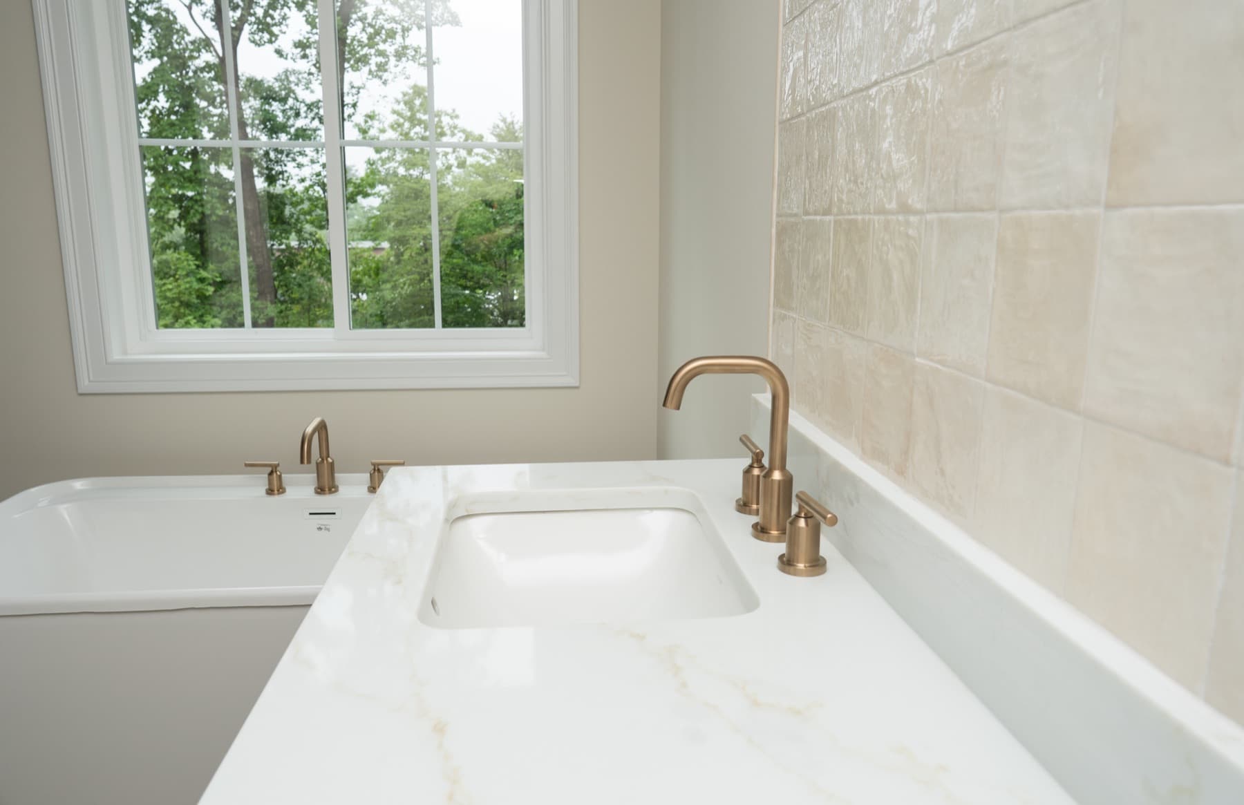 Brass faucet and Jasper quartz vanity top beside a freestanding tub and window